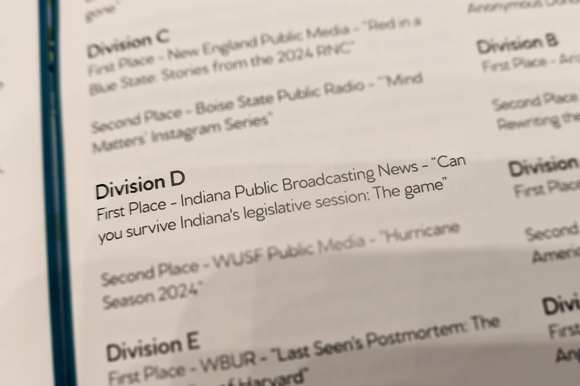 The 2025 PMJA Awards list. All the other entries have been blurred slightly. At the center the text says, 'Division D. First Place - Indiana Public Broadcasting News - 'Can you survive Indiana's legislative session?: The game'